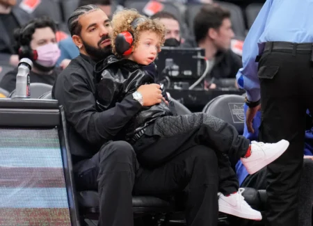 Drake sits with his son Adonis before the Toronto Raptors play the Philadelphia 76ers in their basketball game