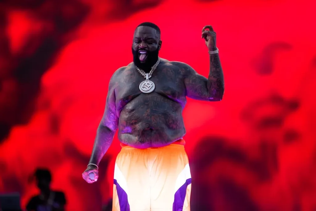 Rick Ross brings big energy under red lights, wearing a chain necklace.